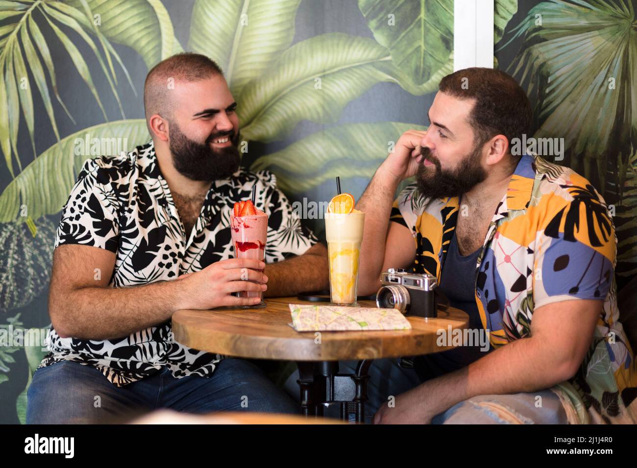 Giovane coppia turistica gay che ha un cocktail in un bar tropicale sulla spiaggia. Viaggio, vacanza e concetto estivo. Foto Stock