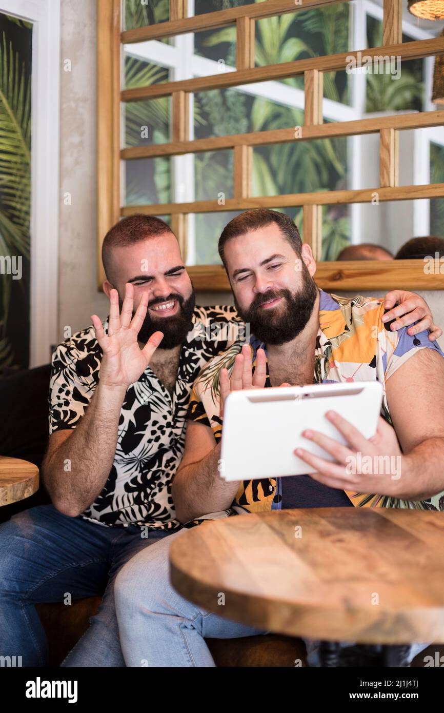 Sorridendo una coppia gay in vacanza facendo una videochiamata da un tablet. Concetto di connessioni remote. Spazio per il testo. Foto Stock