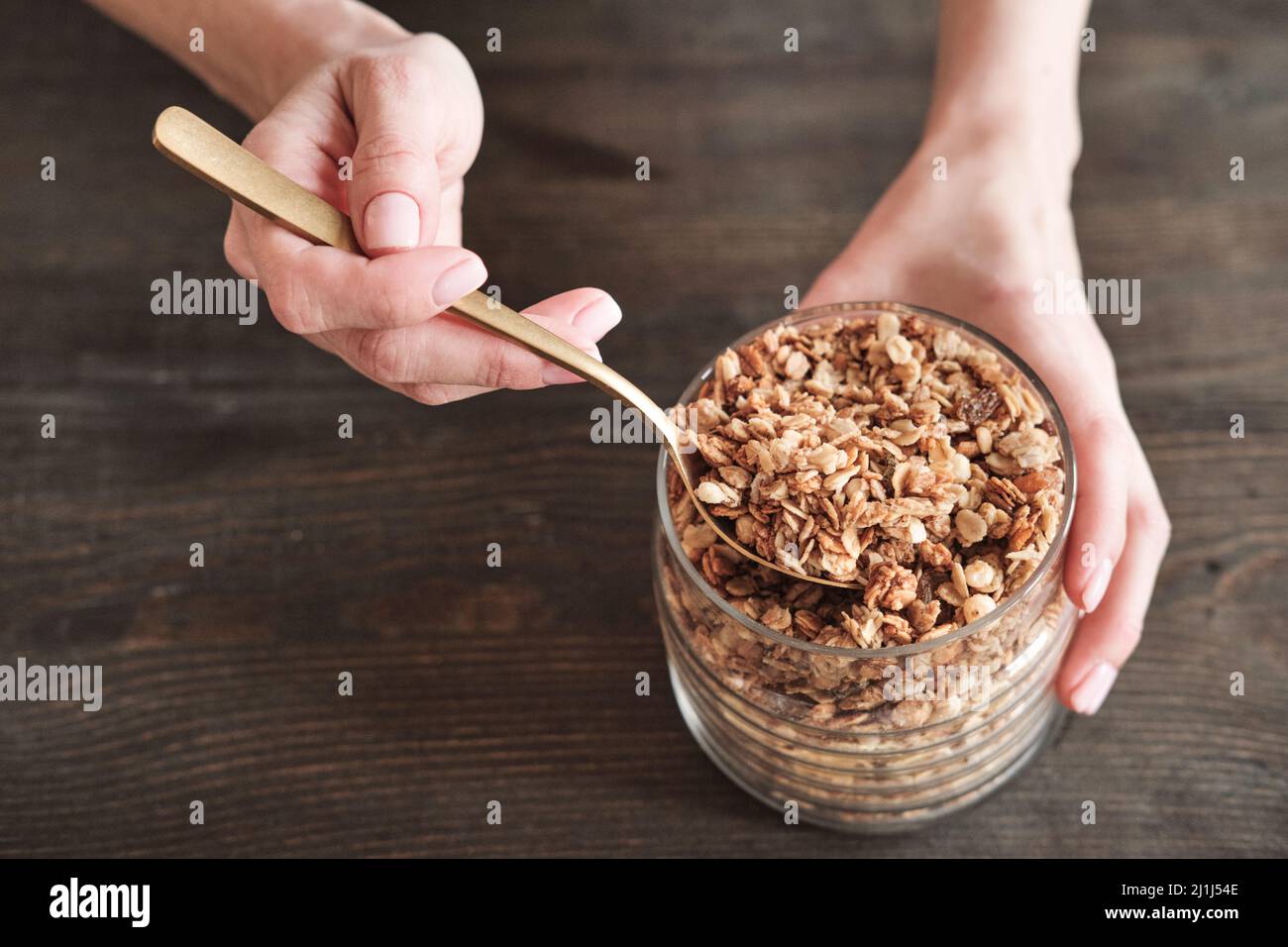 Primo piano di una donna irriconoscibile con vasetto naturale che tiene e usa cucchiaio per muesli Foto Stock