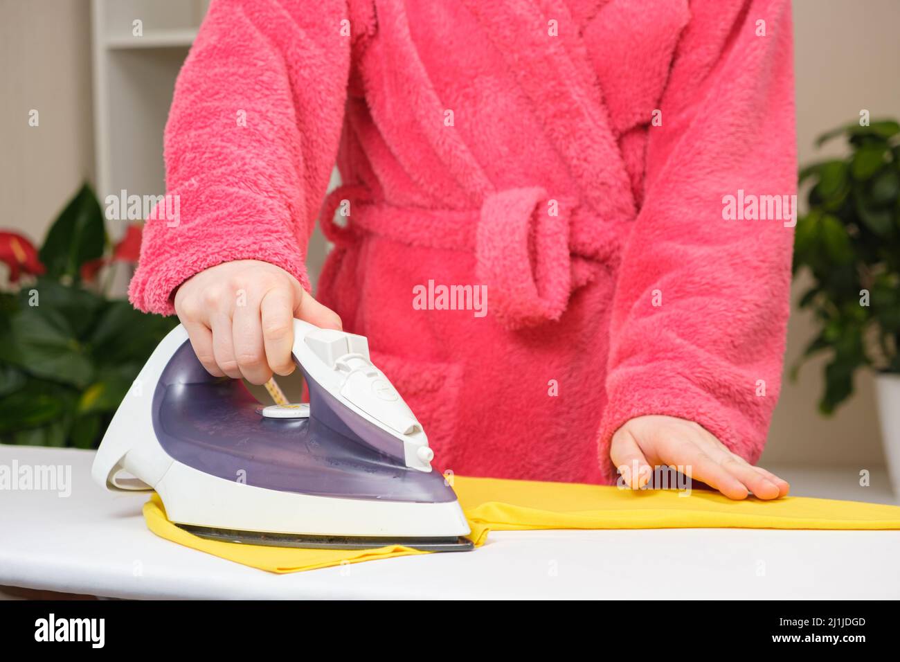Una casalinga in un accappatoio rosa stiratura vestiti., cura per i vestiti. Foto Stock