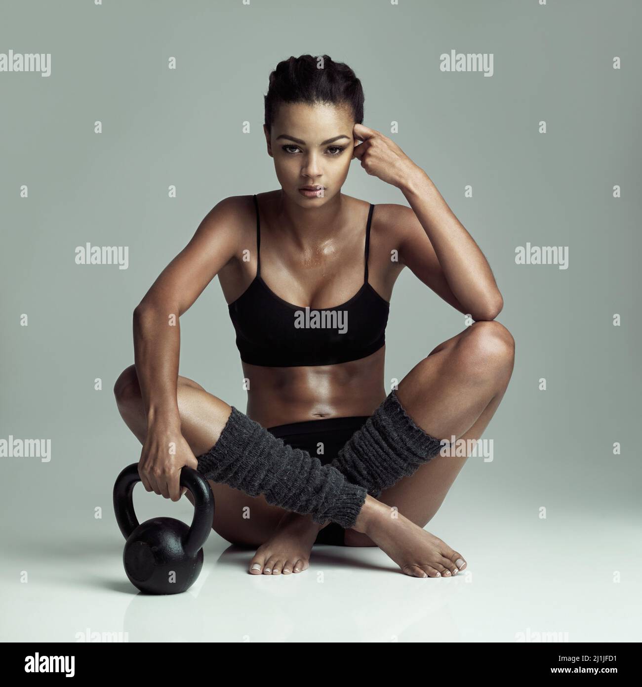 Presa di uno sfiatatoio. Studio girato di una giovane donna in forma seduta sul pavimento con una campana bollitore su sfondo grigio. Foto Stock