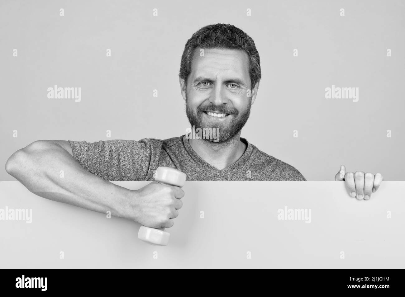 felice uomo bearded dietro carta gialla tenere strumento barbell fitness per spot di formazione, pubblicità Foto Stock