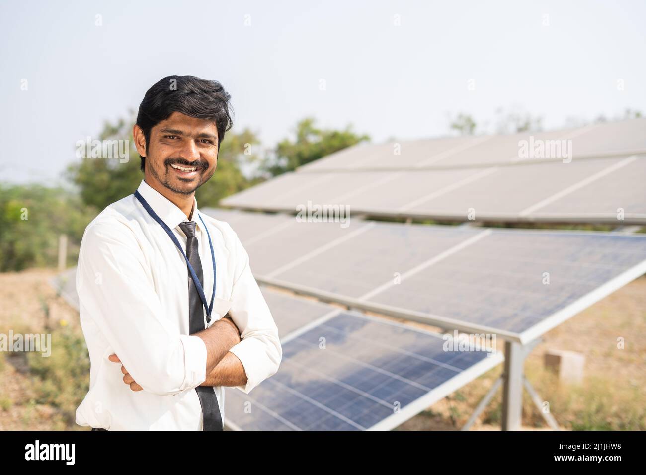 Sorridente ufficiale di banca in piedi con le braccia incrociate guardando la macchina fotografica di fronte ai pannelli solari - concetto di successo, energia rinnovabile e investimenti Foto Stock