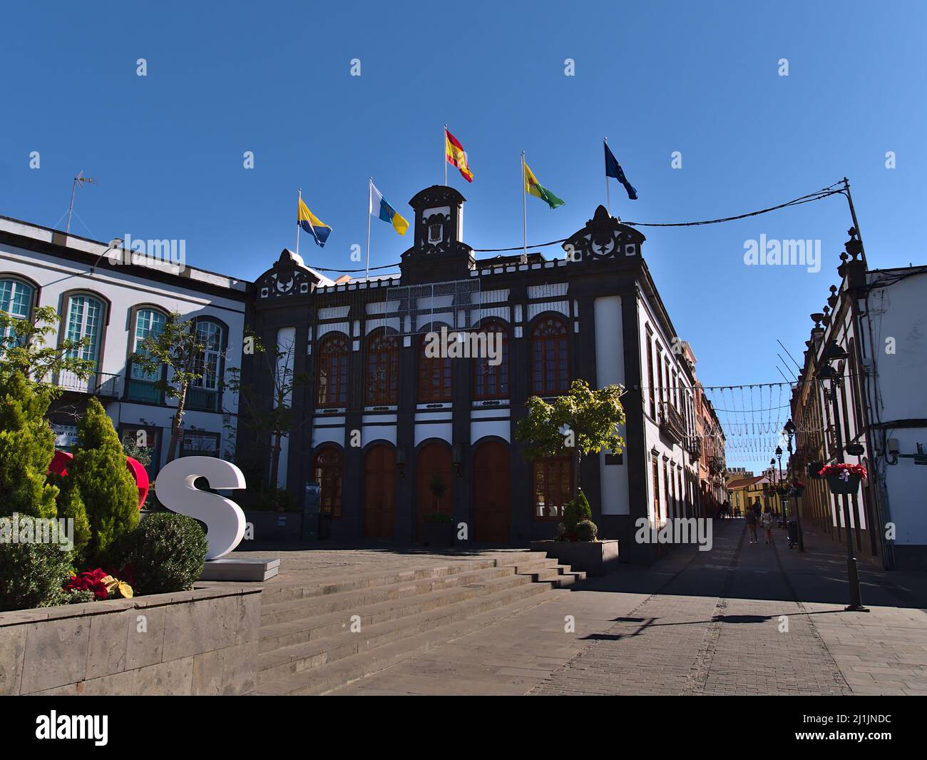 Vista della famosa piazza Plaza de la Constitucion nel centro storico di Arucas, Gran Canaria, Spagna con bandiere su vecchio edificio in giornata di sole. Foto Stock