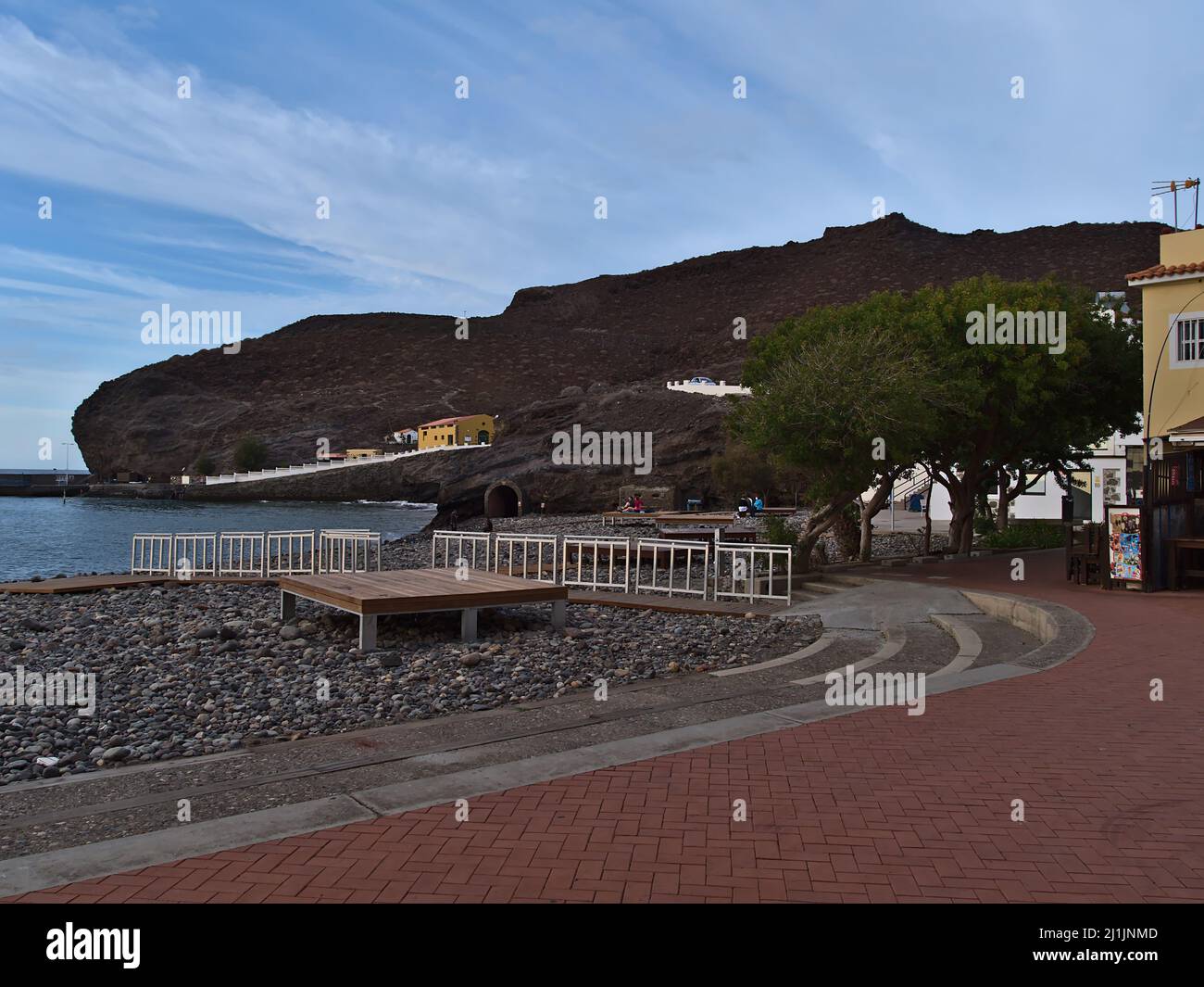 Vista della spiaggia di pietra di la Aldea de San Nicolas, Gran Canaria in serata con passeggiata, edifici e rocce nella stagione invernale. Foto Stock