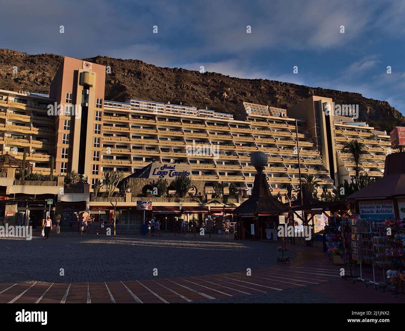 Vista frontale del popolare Hotel Paradise Lago Taurito situato in una valle nel sud di Gran Canaria, Spagna in serata con negozi e persone a piedi. Foto Stock