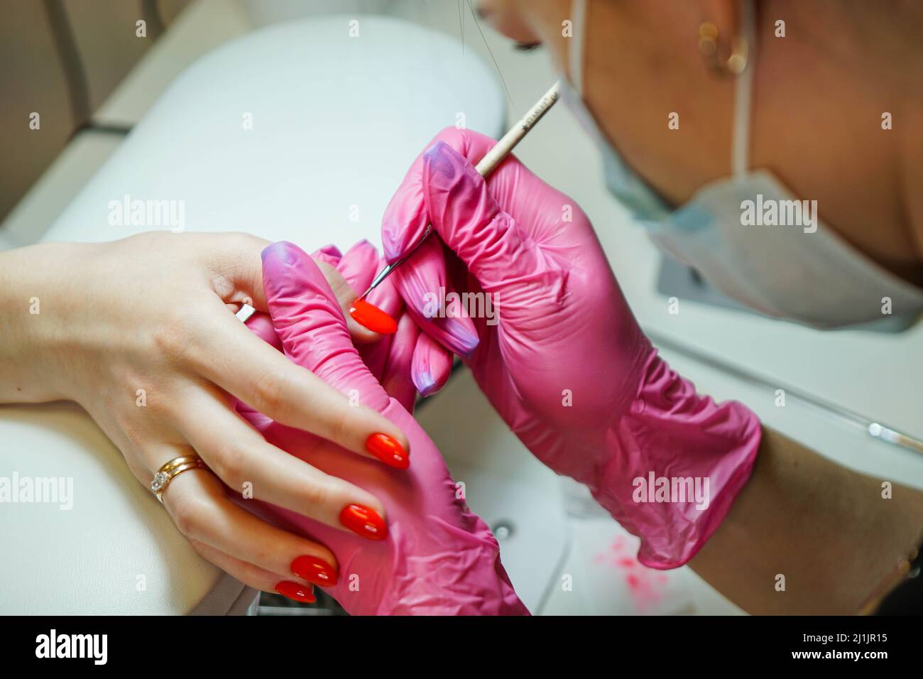 Primo piano del maestro manicure in guanti di gomma che applicano unghie rosse nel salone di bellezza. Foto Stock