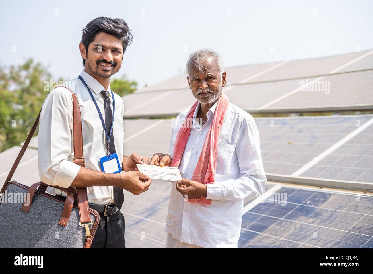 Villaggio agricoltore che riceve assegno da banchiere di fronte al pannello solare - concetto di sostegno finanziario per la produzione di energia rinnovabile, prestito agricolo Foto Stock