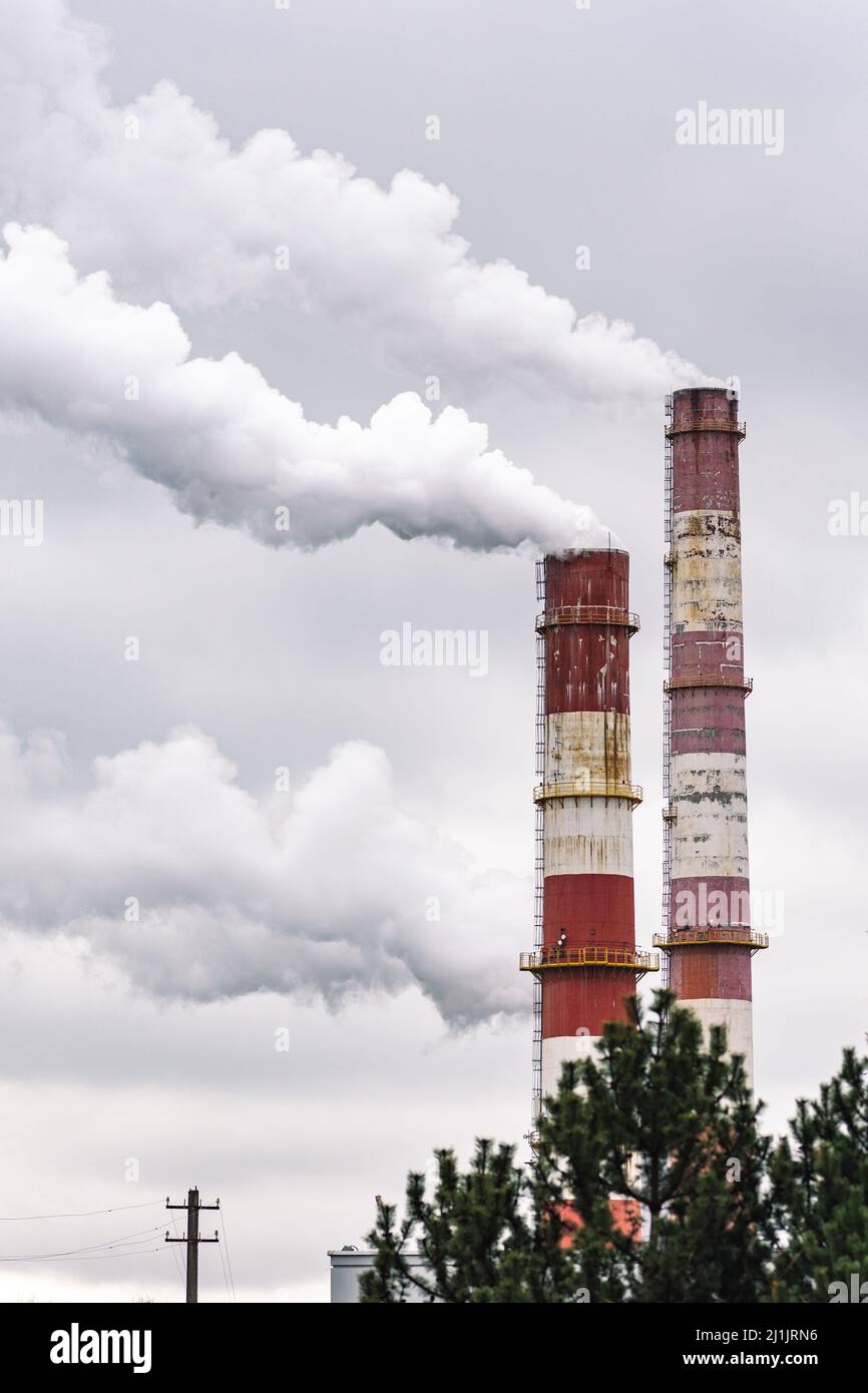 Fumo bianco spesso da fabbrica industriale vecchi camini arrugginiti su sfondo cielo grigio nuvoloso, verticale Foto Stock