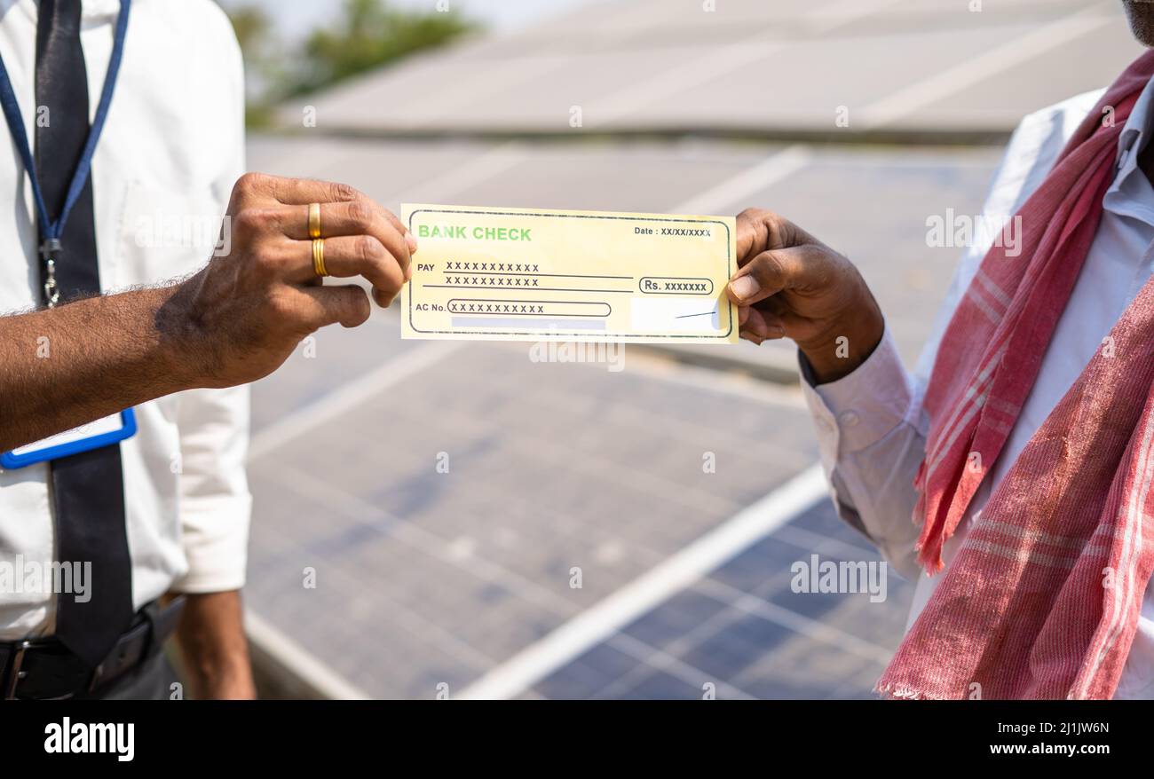 primo piano dell'agricoltore che riceve assegni dal banchiere di fronte al pannello solare - concetto di sostegno finanziario per la produzione di energia rinnovabile Foto Stock