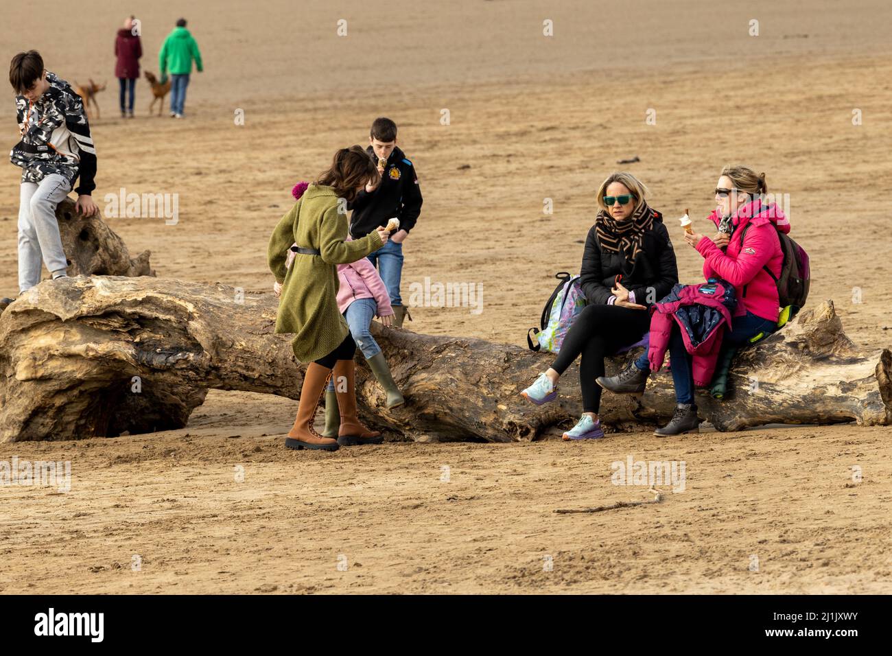 Una famiglia seduta su un giornale in una giornata fredda in spiaggia Foto Stock