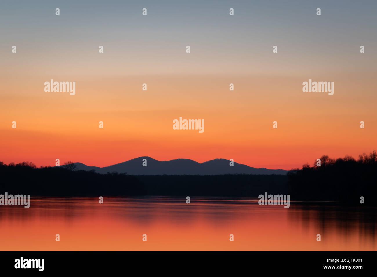 Paesaggio del fiume Sava, foreste e silhouette di montagna lontane, cielo limpido con vibrante luce rossa e arancione all'orizzonte durante il crepuscolo Foto Stock