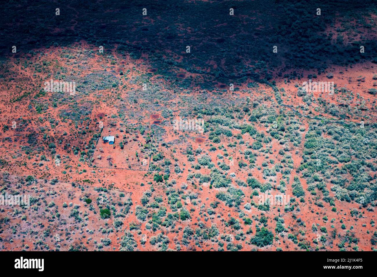 Vista aerea di una semplice fattoria e casa di famiglia nella zona tribale di Maasai del Kenya e l'ombra di una grande nuvola che oscura la terra arida e arida Foto Stock
