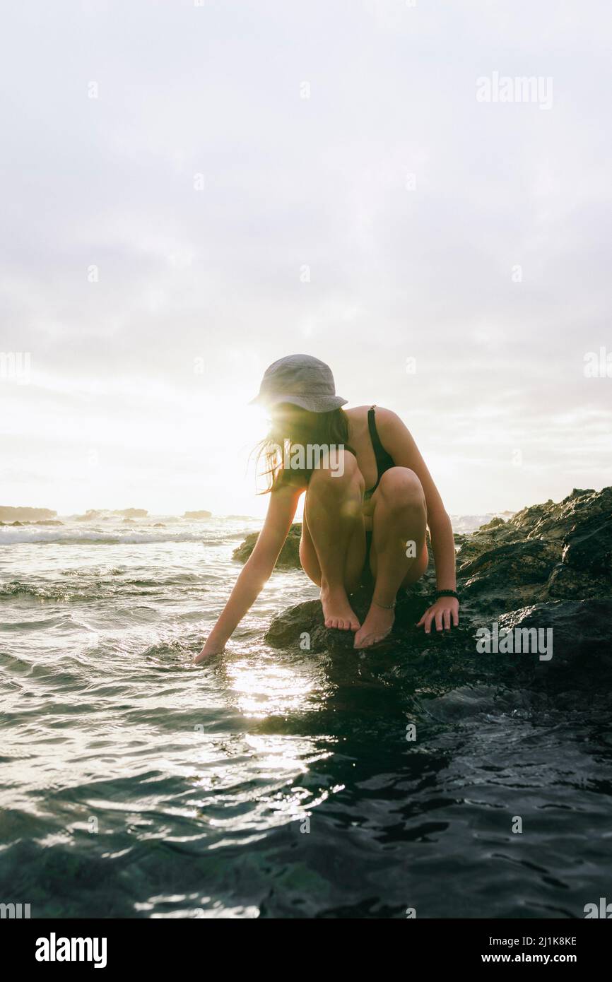 donna sulla spiaggia durante il tramonto, toccando l'acqua Foto Stock