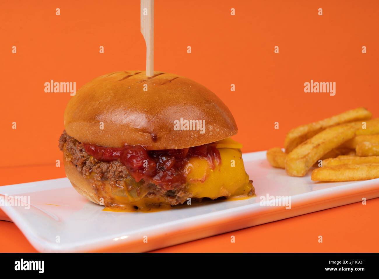 Una vista laterale di un piatto di hamburger e patatine fritte su sfondo arancione. Foto Stock