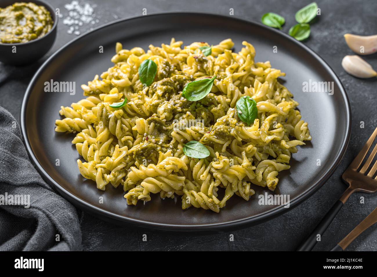 Pasta con salsa di pesto, foglie di basilico fresco e semi di sesamo su sfondo scuro. Vista laterale, primo piano. Foto Stock