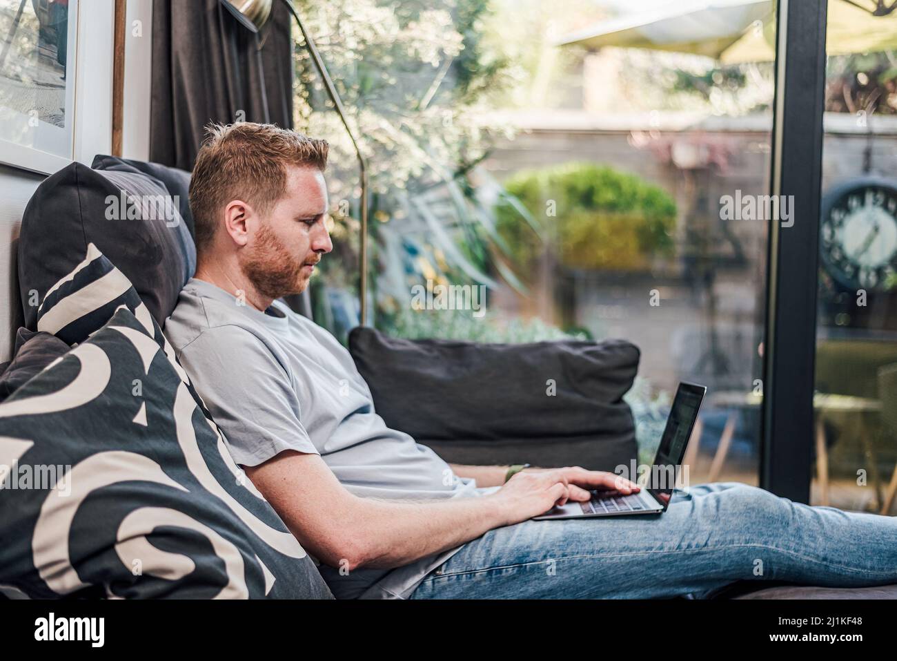 Uomo adulto serio, seduto sul divano, usando il suo laptop, navigando online. Foto Stock