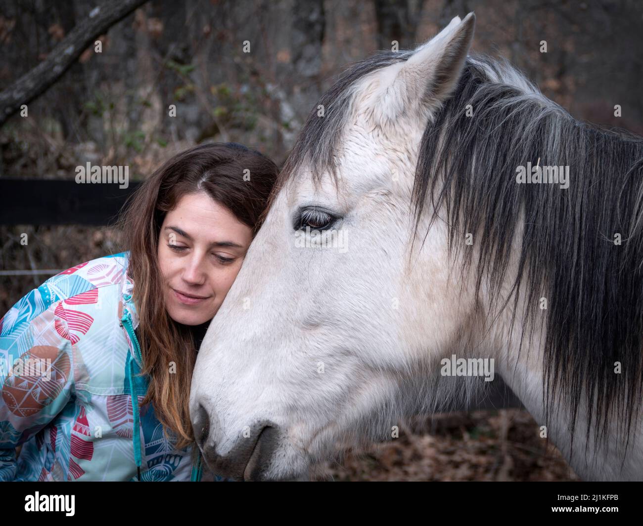 Donna brunetta con un aspetto triste e romantico sul suo viso e il suo cavallo bianco in una giornata d'inverno. Foto Stock