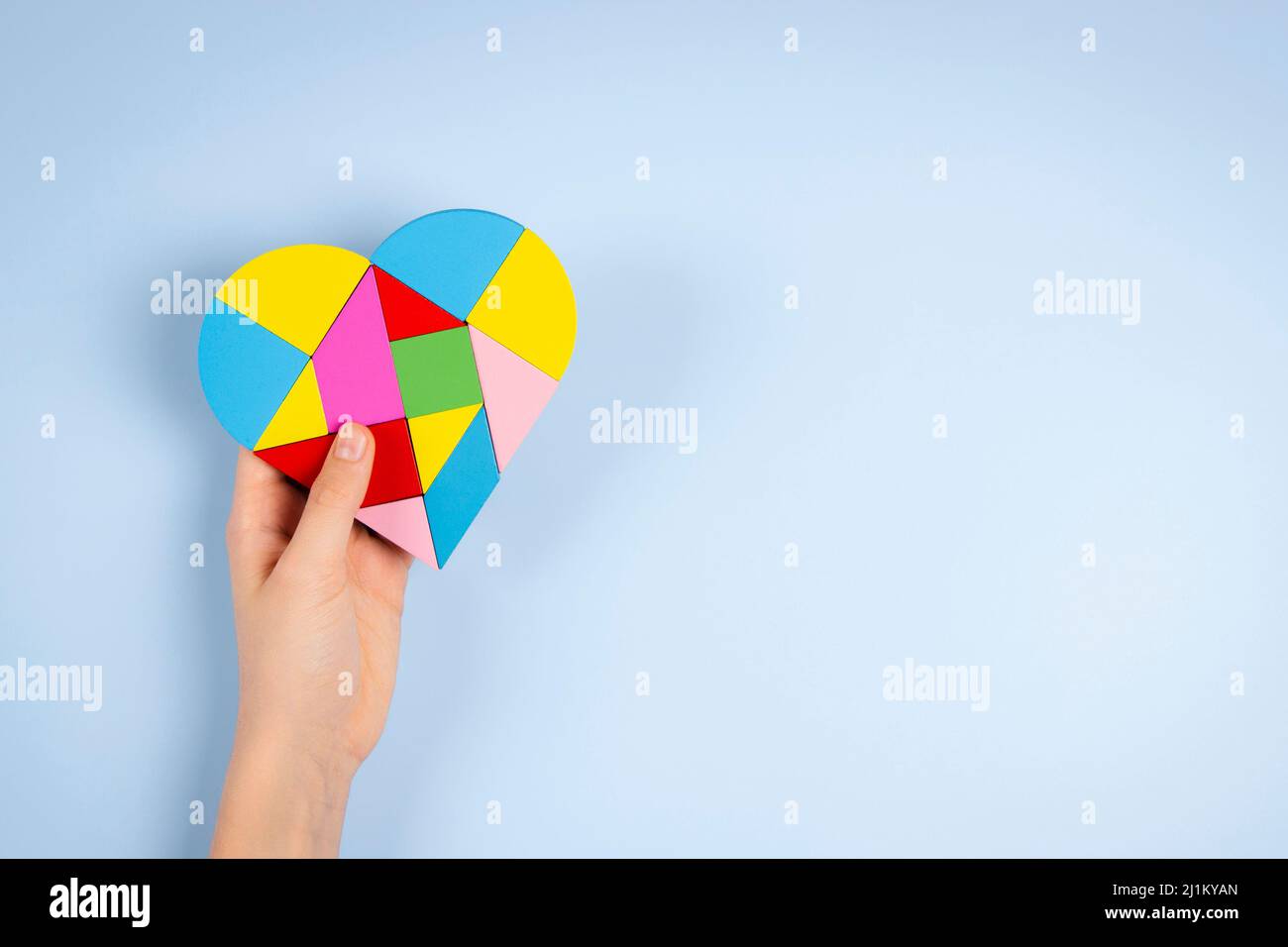 Bambino mano che tiene colorato puzzle cuore su sfondo azzurro chiaro. Concetto di giornata di consapevolezza autismo mondiale Foto Stock