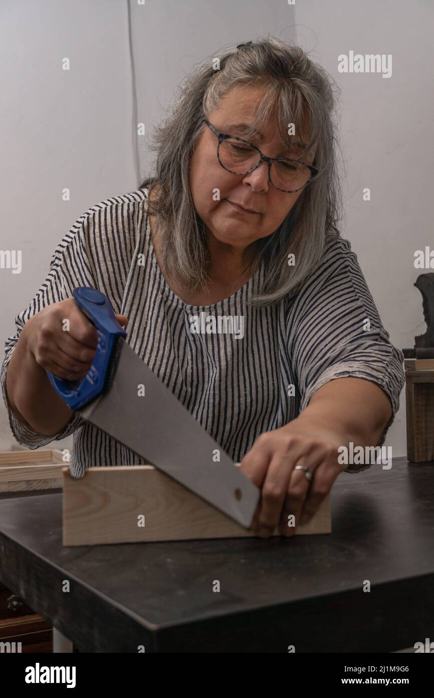 donna dai capelli bianchi al lavoro nella sua officina di legno riciclato Foto Stock