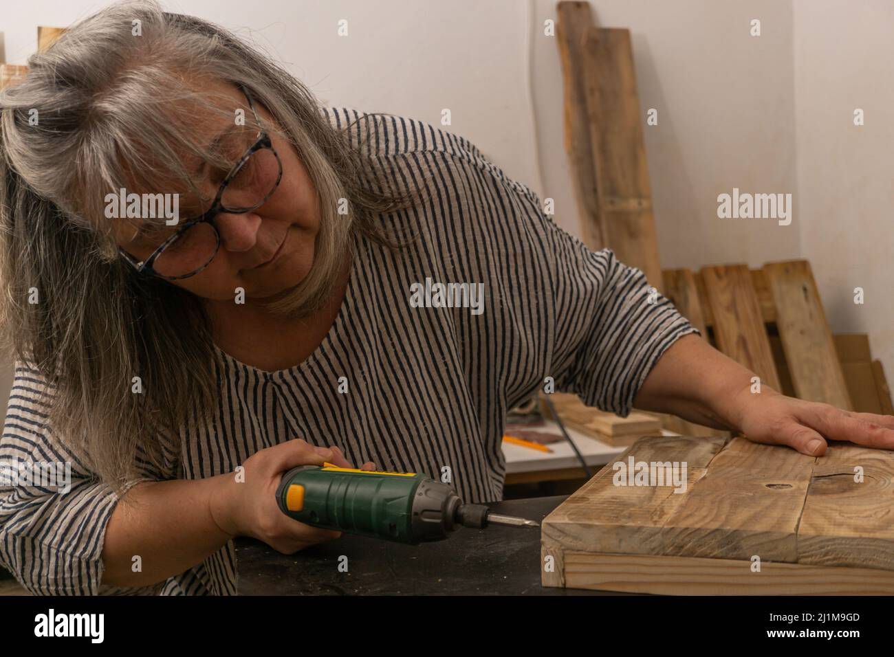 donna dai capelli bianchi al lavoro nella sua officina di legno riciclato Foto Stock