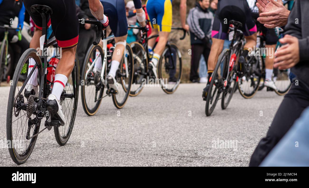 Vista posteriore di un gruppo di ciclisti irriconoscibili in pieno sforzo fisico con il pubblico che li acclamano. Foto Stock