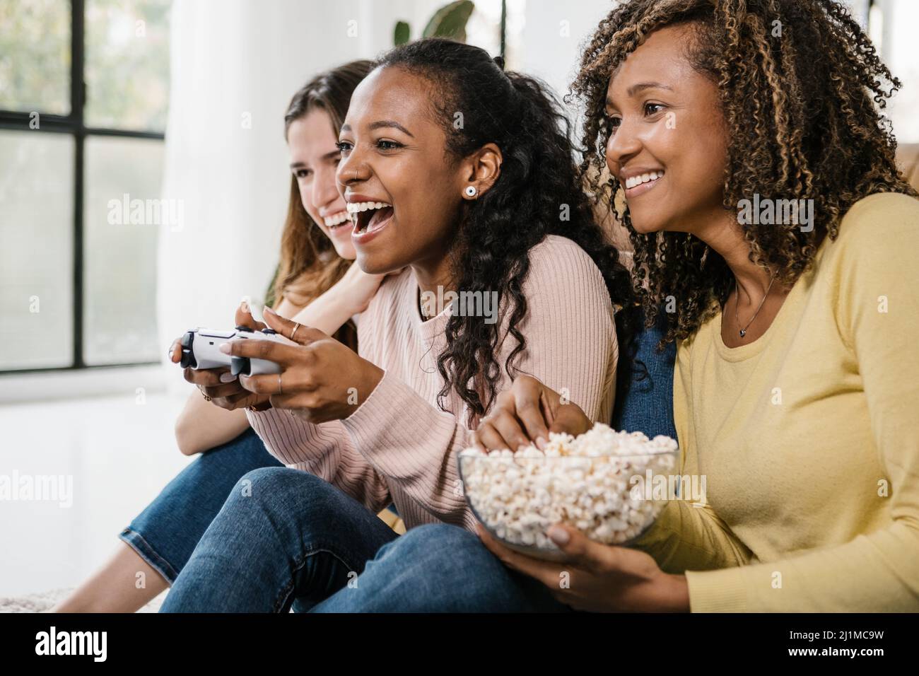 United multirazzial giovani donne che giocano videogiochi con console a casa Foto Stock