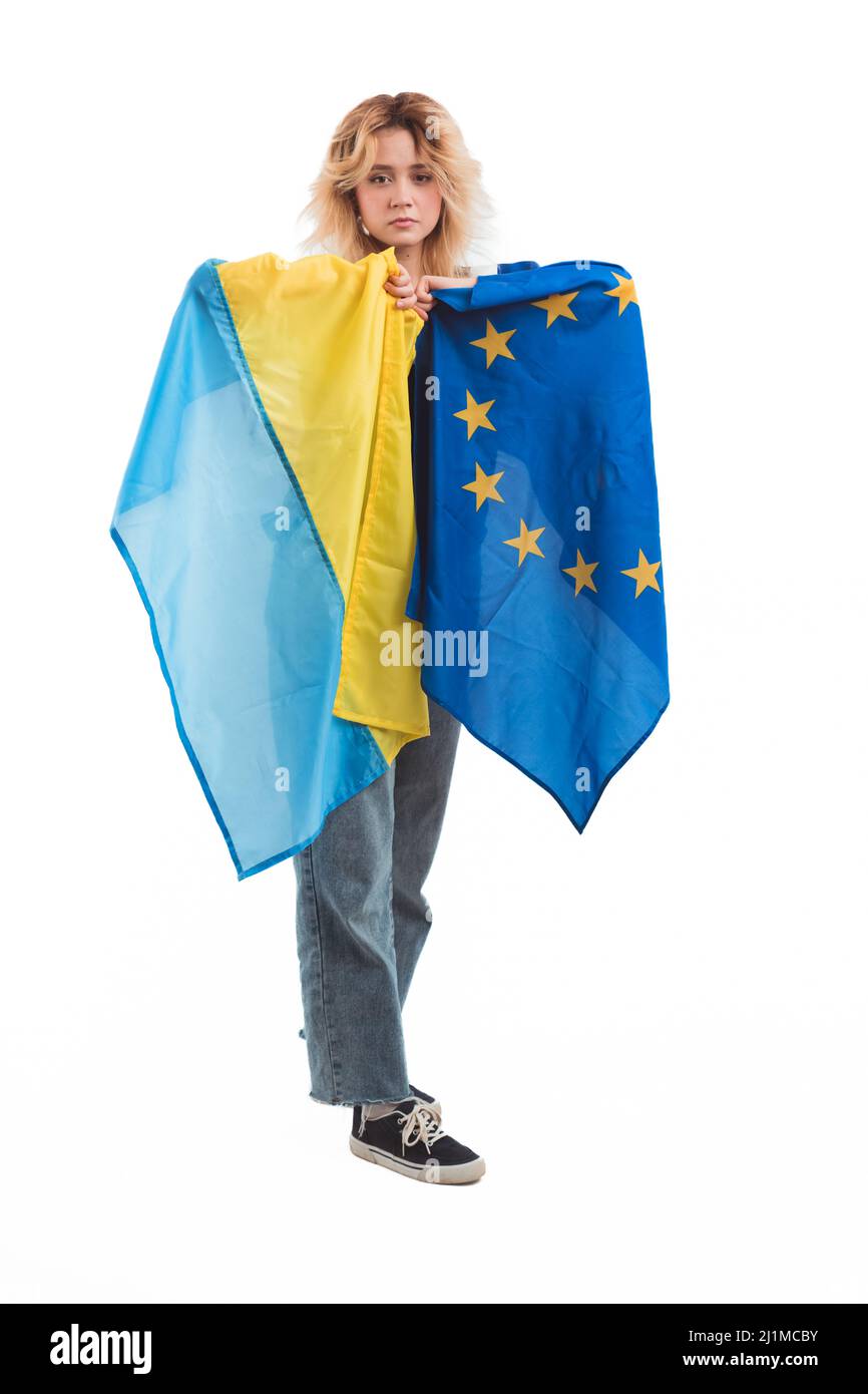 Orgogliosa e sconvolsa donna caucasica dai capelli biondi nel suo 20s tenendo insieme bandiere ucraine ed europee. Europa per l'Ucraina. Studio verticale girato su sfondo bianco. Foto di alta qualità Foto Stock