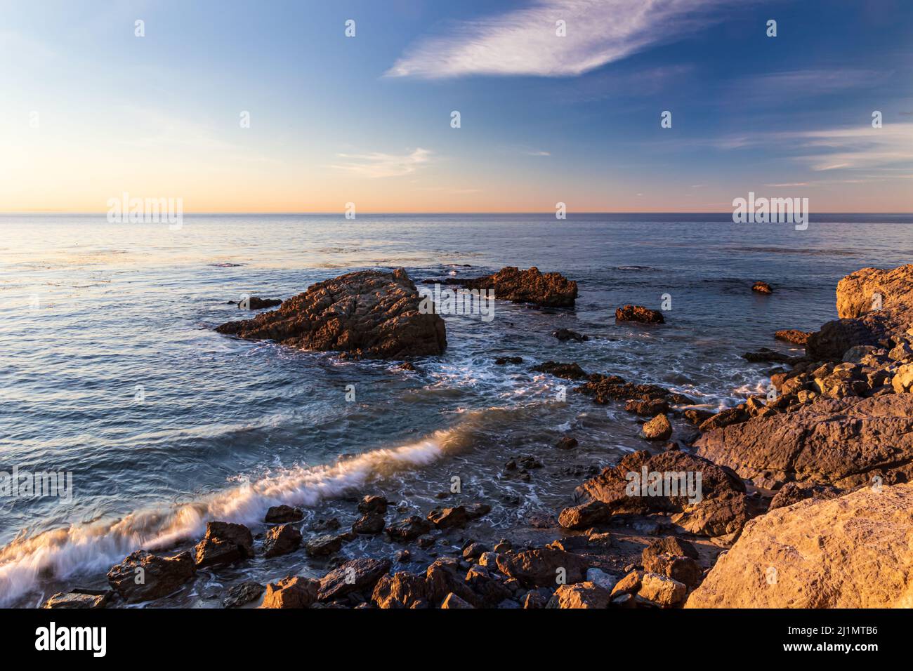 Spiaggia rocciosa a Malibu, California, al mattino presto. Tranquillo oceano Pacifico in lontananza; cielo blu e nuvole in testa. Foto Stock
