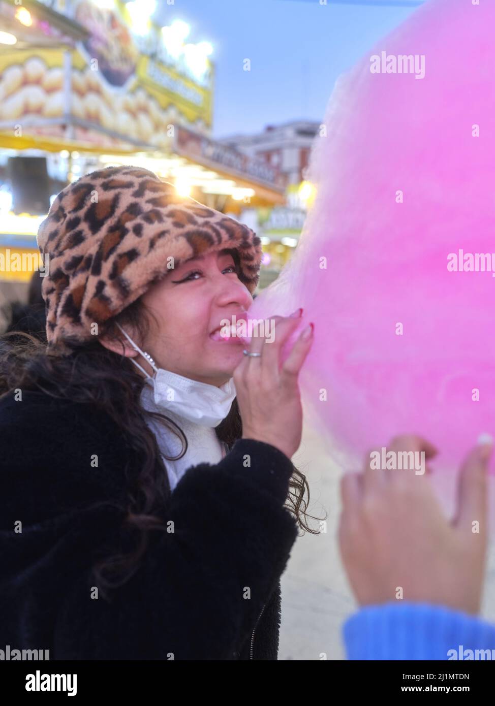 Donna latina mordente un pezzo di caramella di cotone rosa nella notte Foto Stock