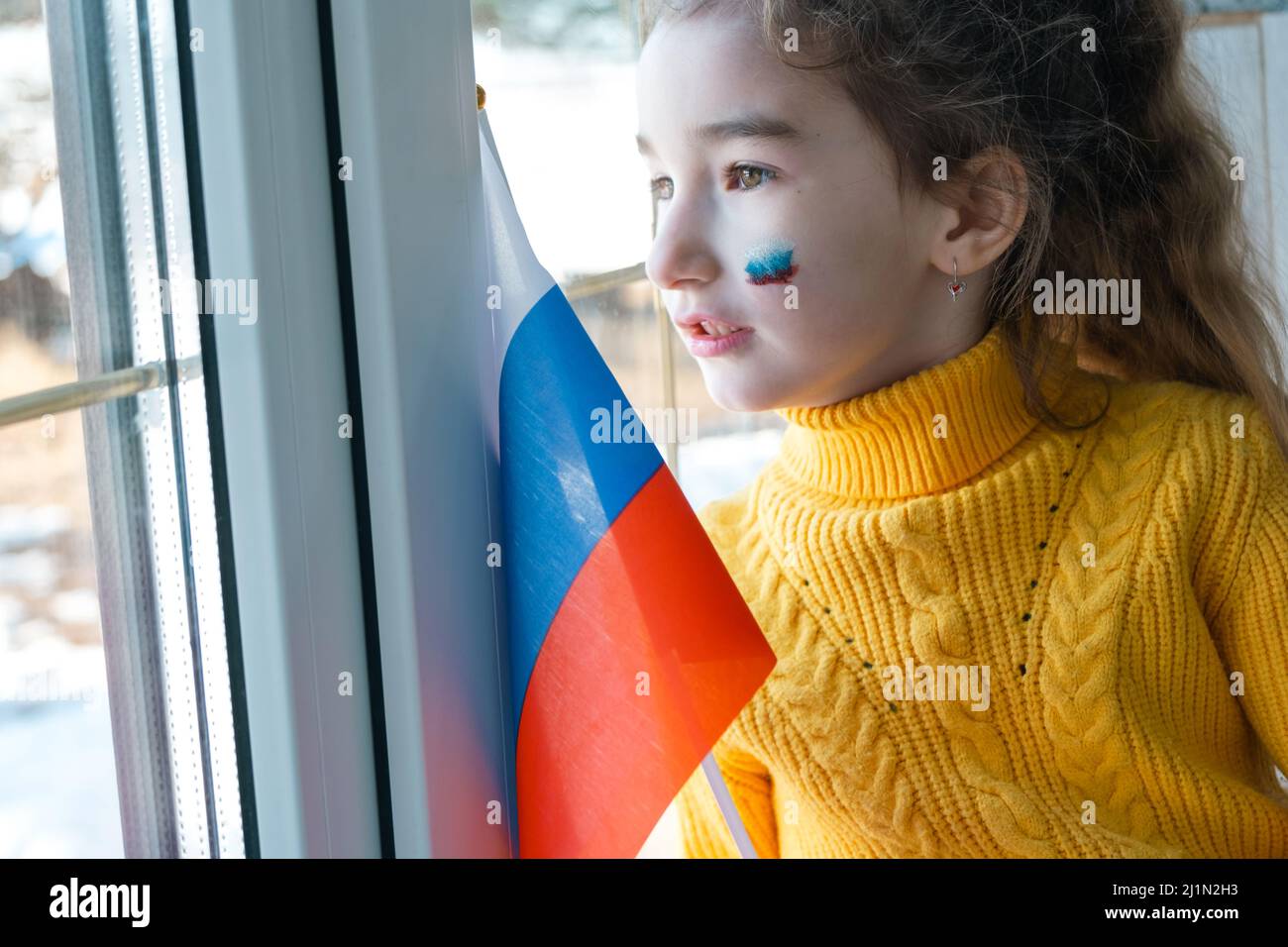 Un bambino triste alla finestra con la bandiera della Russia, si preoccupa di lacrime nei suoi occhi. Conflitto tra Russia e Ucraina, paura Foto Stock