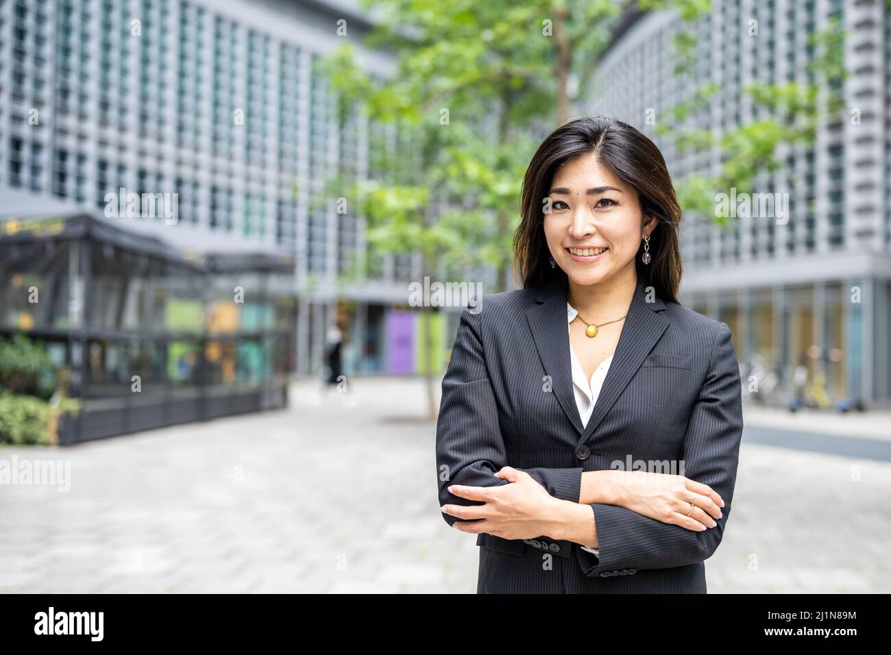 Donna d'affari con le braccia piegate che sorride fiducioso per i suoi successi, icona dell'economia verde, donna d'affari femminile di origine asiatica, copia spac Foto Stock