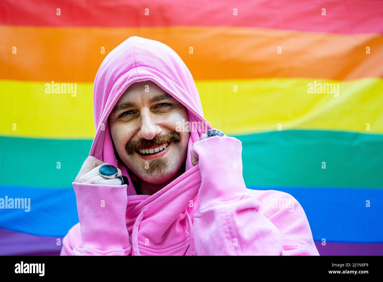 uomo gay felice sorridendo e guardando la macchina fotografica, bandiera arcobaleno sullo sfondo - gay orgoglio celebrazione, inclusione sociale, uguaglianza e diversità concetto Foto Stock