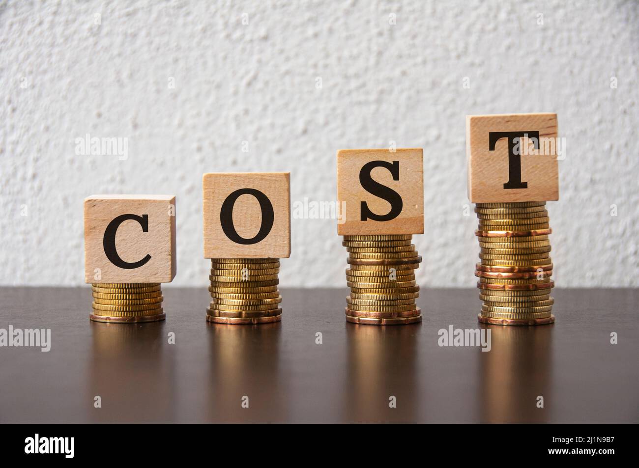 Pila di monete con testo di costo su blocchi di legno - Business e concetto finanziario Foto Stock