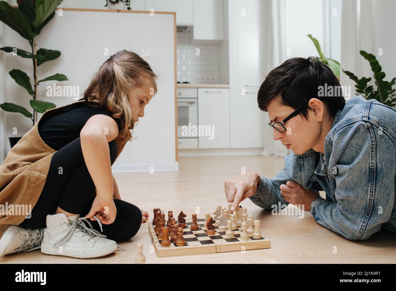 Partita di scacchi competitiva tra papà e sua figlia. Sia eccitato che divertirsi. Vista laterale. Sul piano della cucina. Foto Stock