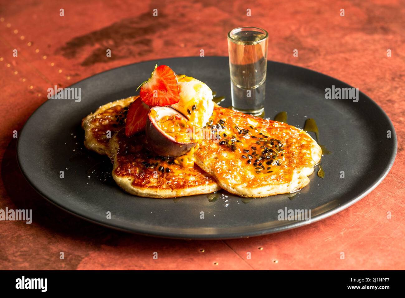 Un primo piano di pancake con fragole, frutto della passione e gelato servito su un piatto nero Foto Stock
