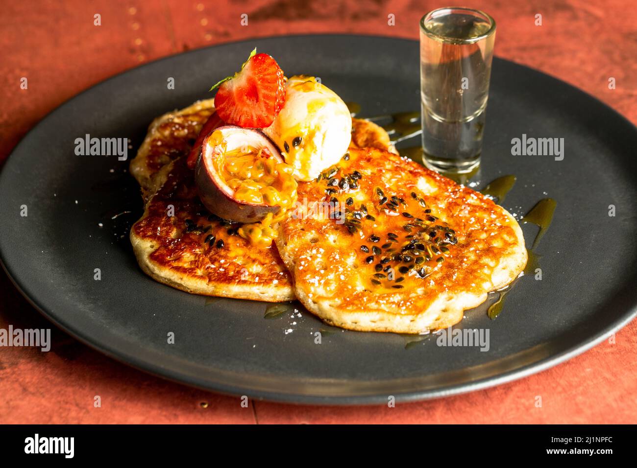 Un Closeup di pancake con fragole, un frutto della passione, e gelato servito su un piatto nero Foto Stock