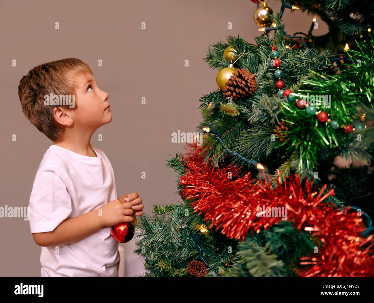 Natale è un momento di meraviglia tipo bambino.... Un ragazzo giovane che decora un albero di Natale. Foto Stock