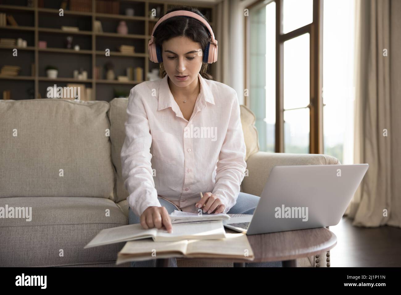 Studentessa seria in grandi cuffie rosa che studiano a casa Foto Stock