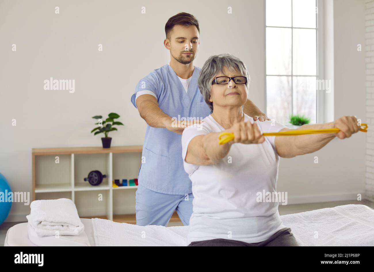 Donna anziana con nastro elastico che fa esercizio di stretching con fisioterapista maschile. Foto Stock