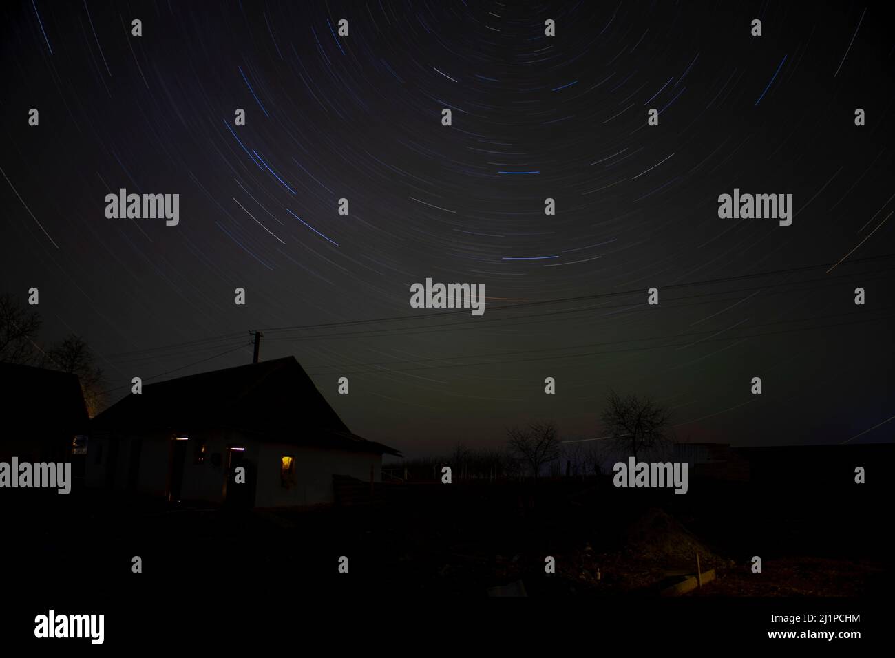 Bellissimo paesaggio notturno, casa, auto e sentieri stellari. Le stelle colorate seguono nel cielo. Riprese notturne intermedie. Foto Stock