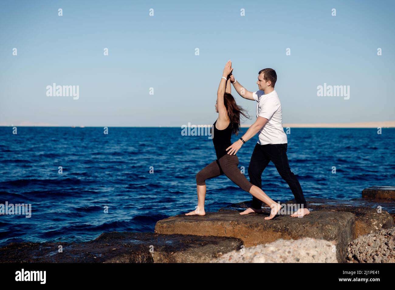 Cliente donna che fa stretching o yoga all'aperto sfondo mare, personal trainer uomo correggere lei. Foto Stock