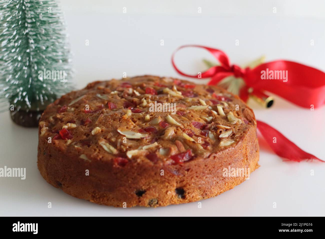 Torta di frutta con rum imbevuto di frutta e noci preparato per natale. Girato con albero di Natale, cornici di pino e nastri decorativi sullo sfondo Foto Stock