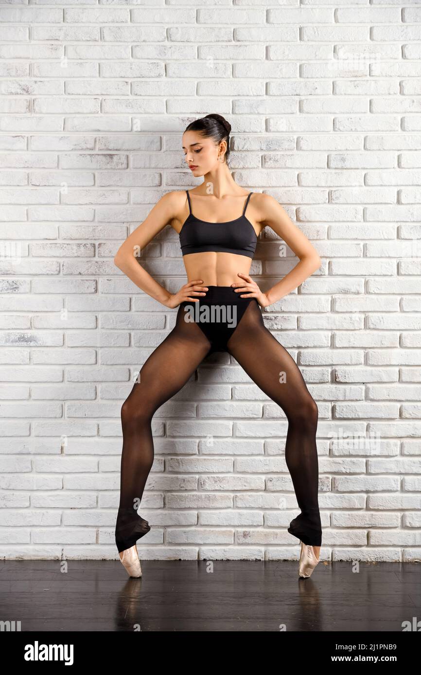 Corpo completo di ballerina in punta scarpe equilibrate su tittoes e appoggiate su muro di mattoni bianchi nella sala da ballo Foto Stock