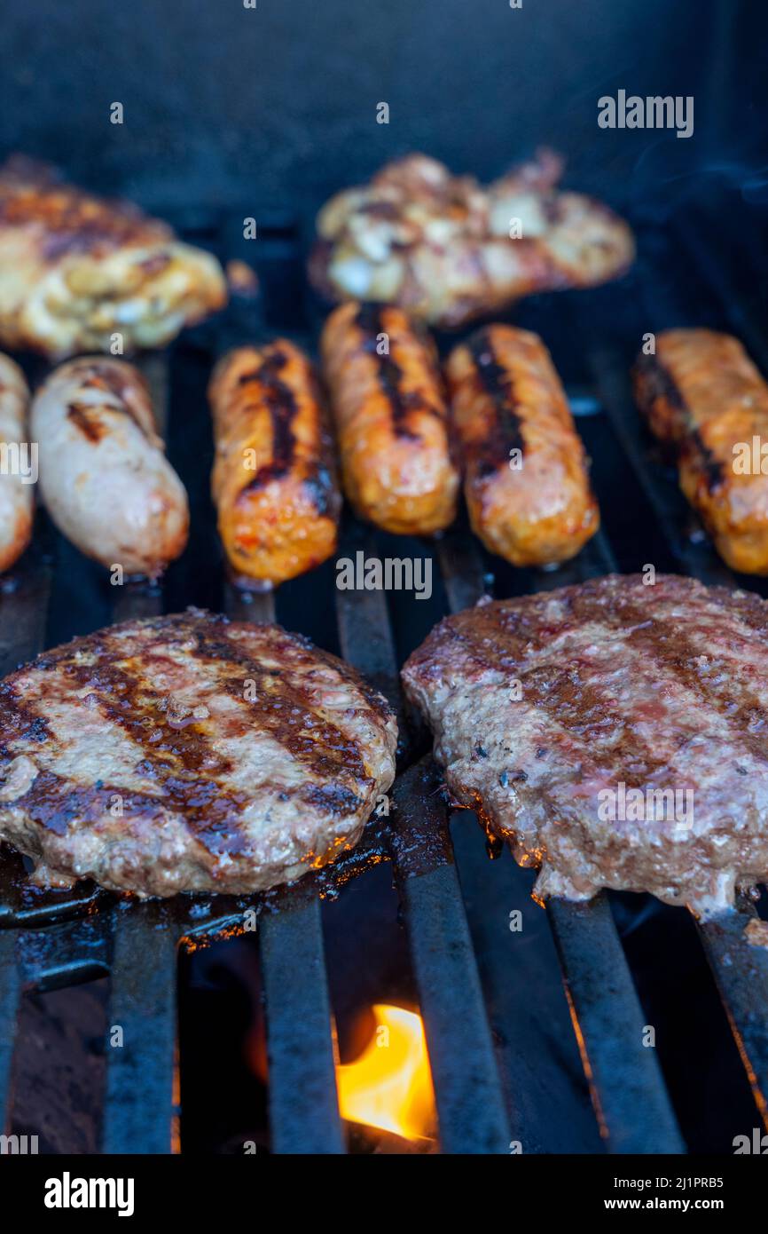 Hamburger e salsicce sfrigolanti su un barbecue Foto Stock