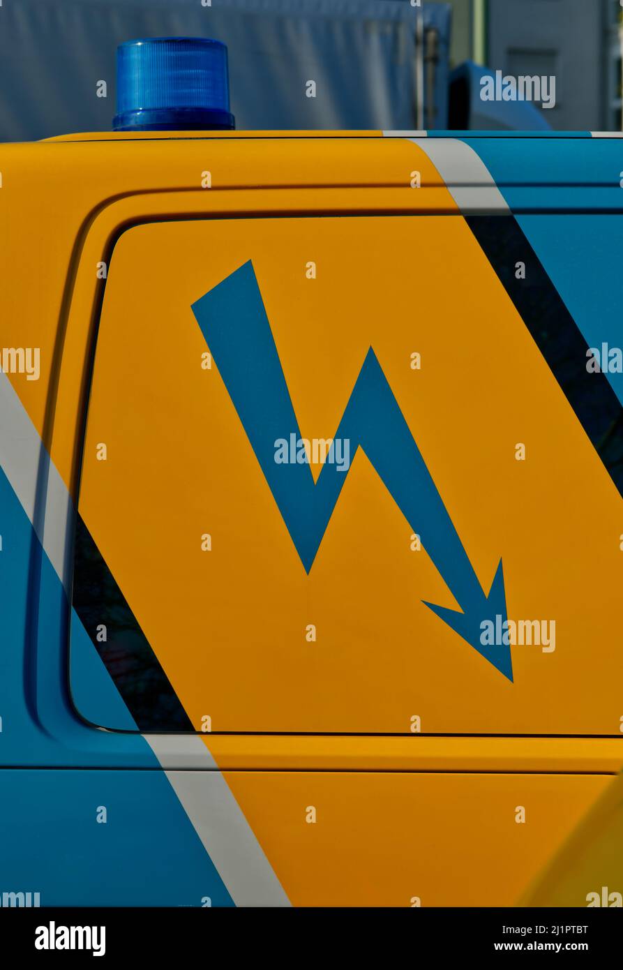parte posteriore di un'auto di emergenza con luce blu e un segno di un lampo elettrico dipinto in blu su terreno giallo Foto Stock