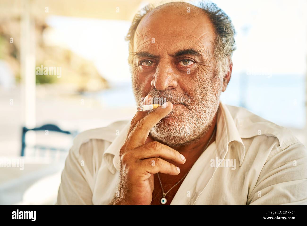 È un ragazzo duro. Ritratto di un uomo anziano sicuro che fuma una sigaretta e si alza all'esterno mentre guarda la macchina fotografica. Foto Stock