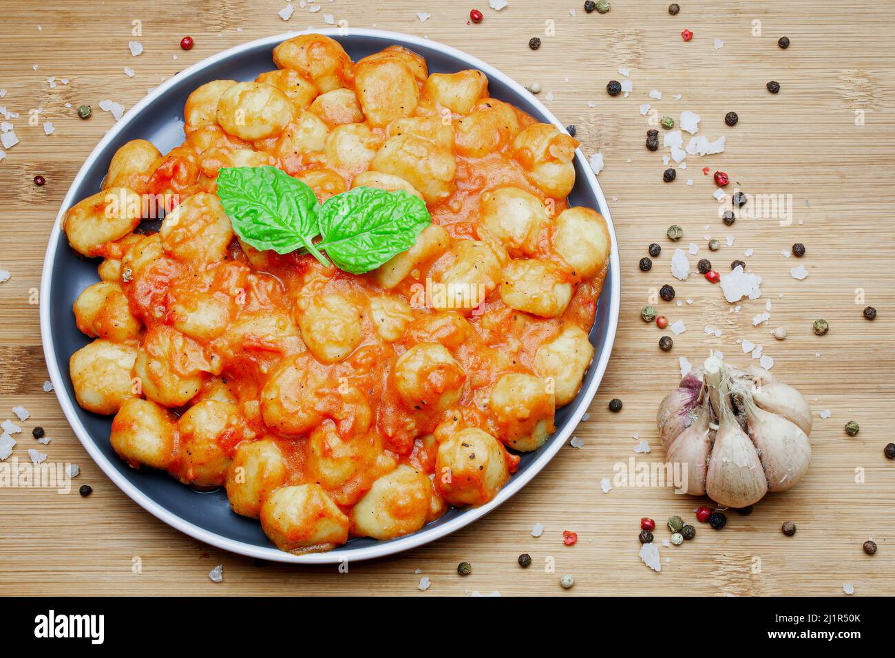 Gnocchi italiani fatti in casa in salsa di pomodoro aromatica serviti su un piatto decorativo e guarniti con erbe, basilico, pepe colorato, aglio e. Foto Stock