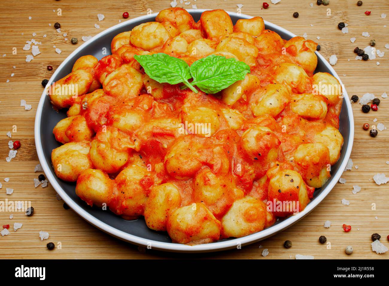 Gnocchi italiani fatti in casa in salsa di pomodoro aromatica serviti su un piatto decorativo e guarniti con erbe, basilico, pepe colorato, aglio e. Foto Stock