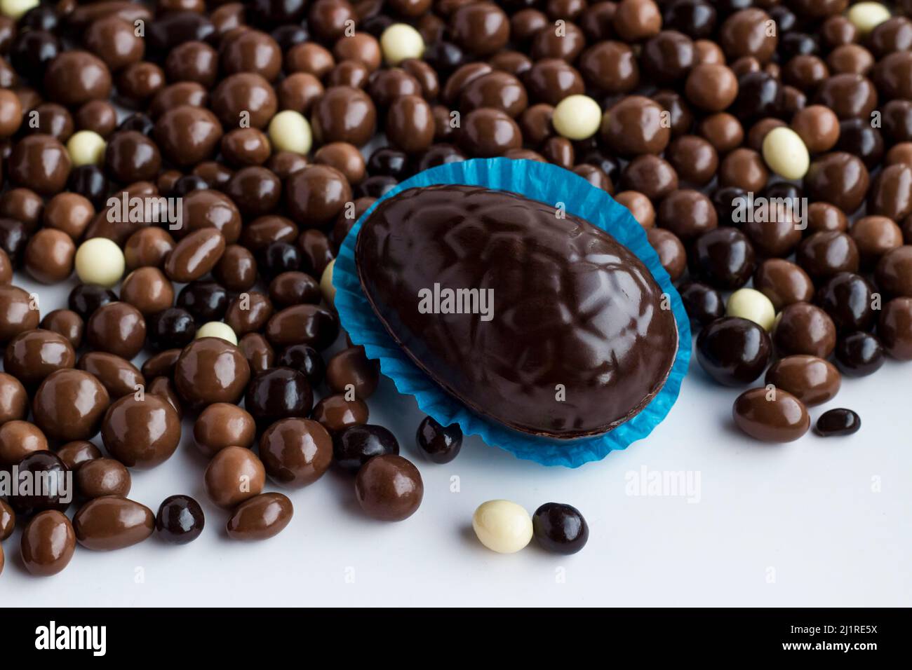 Uovo di cioccolato fondente in cupcake di carta blu con cioccolato fondente e marrone palla su superficie bianca. Concetto di festa di Pasqua Foto Stock